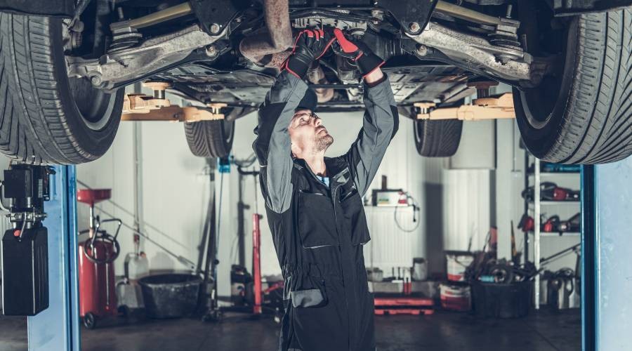 Automonteur aan het werk in de garage De onderkant van de auto wordt nagekeken
